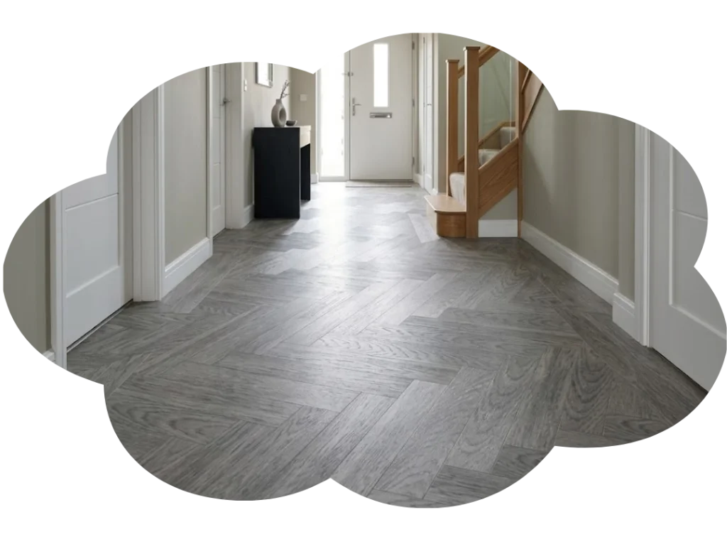 Modern hallway with gray herringbone wood flooring, white walls, and wooden staircase leading upstairs.